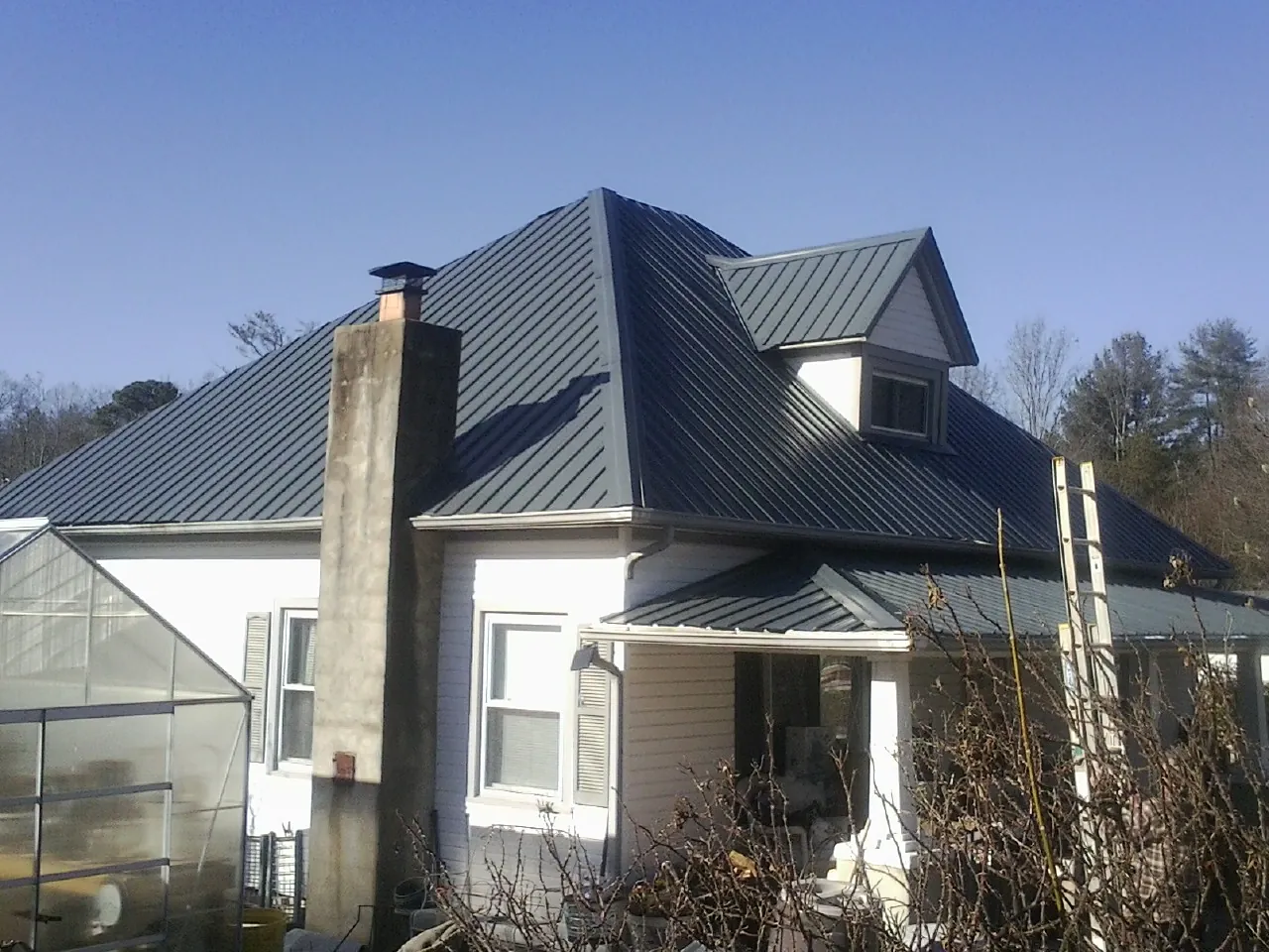 Dark blue standing seam metal roof on a white farmhouse with dormer — Slate & Tile Roof Repair by Roofing Brothers in Chugwater