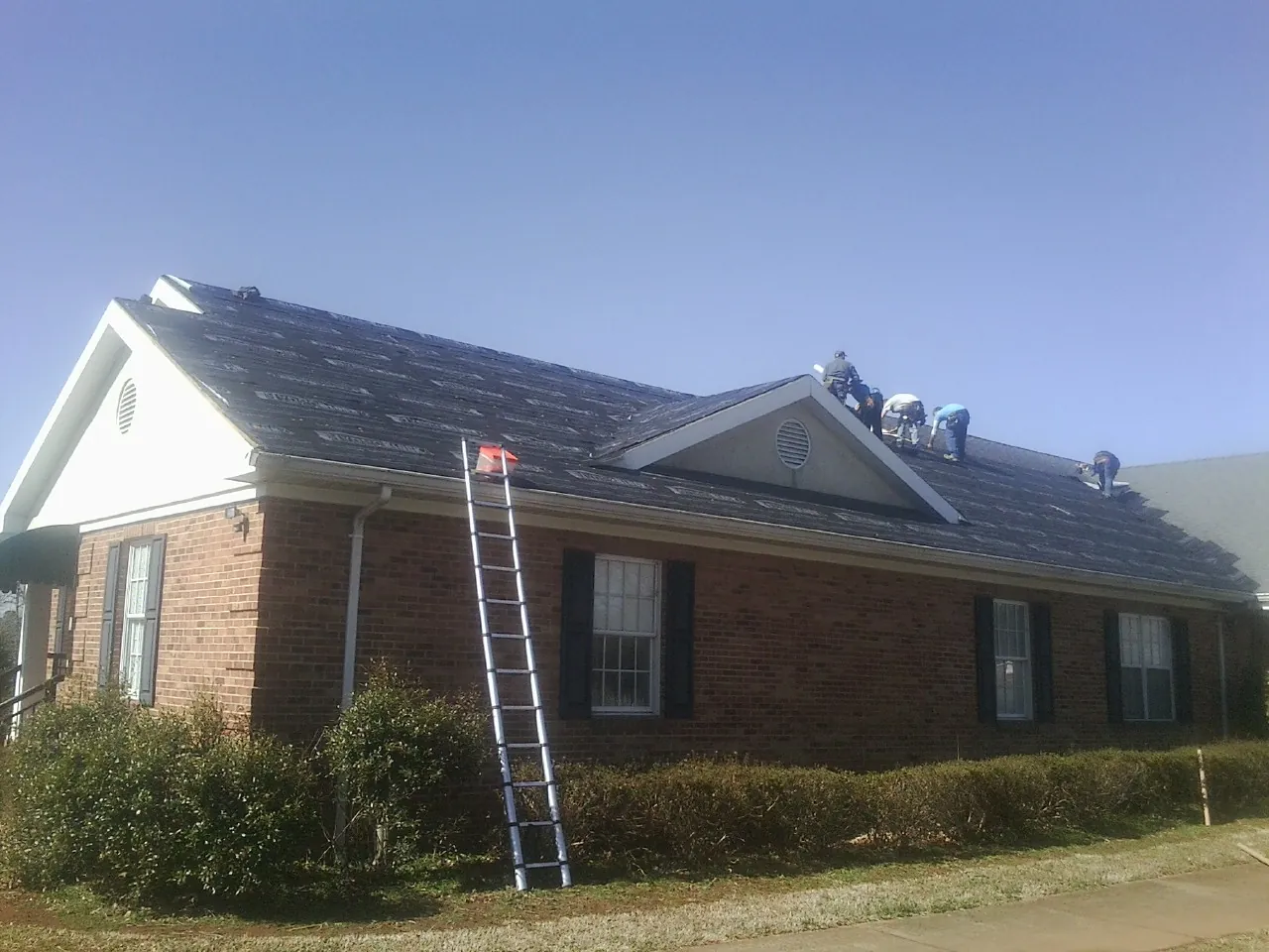 Crew tearing shingles off a brick ranch roof with a ladder set — Metal Roof Repair work by our crew in Chugwater