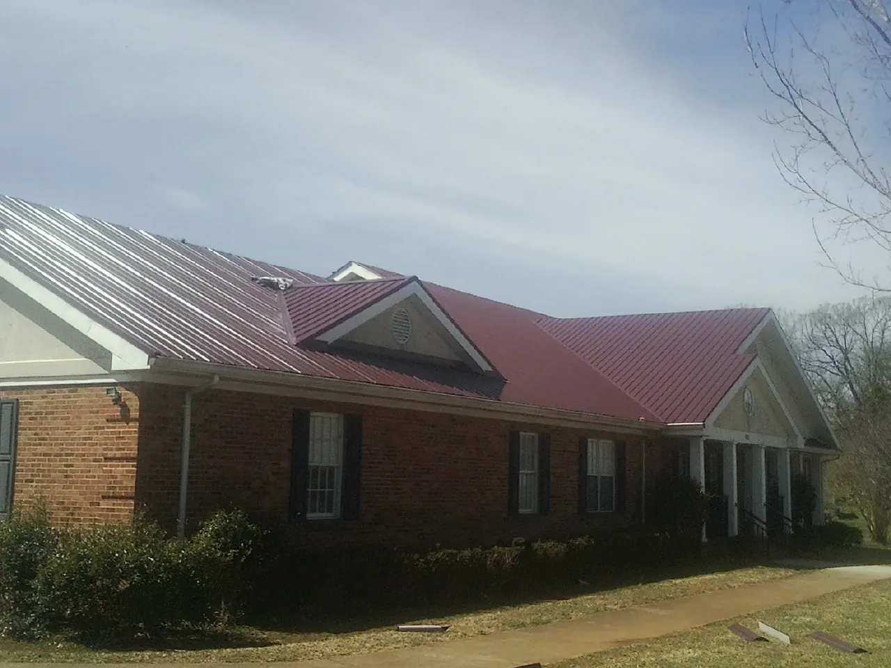 Red metal roof with gabled entries on a long brick building, from a Hail Damage Roof Repair job in Chugwater