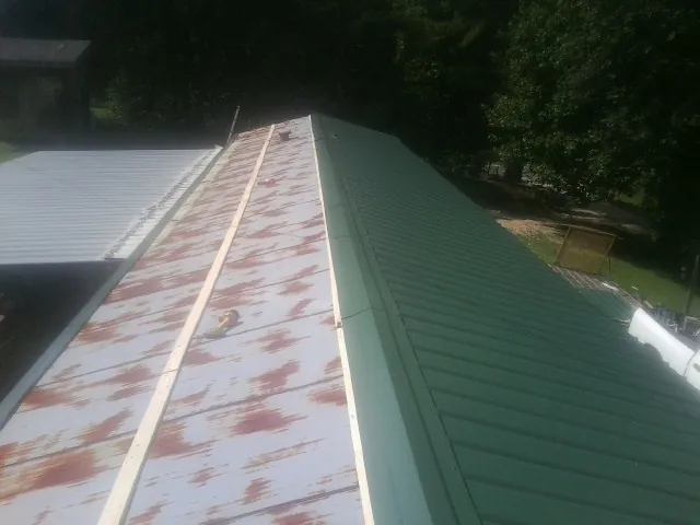Old rusted panels beside newly installed green metal roofing — Wind Damage Roof Repair by Roofing Brothers in Chugwater