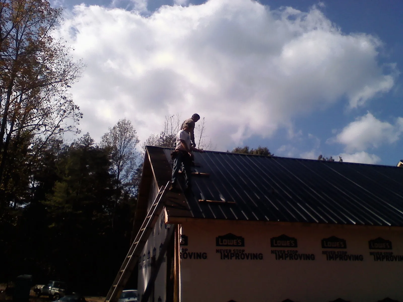 Roofer fastening dark metal panels high against a cloudy sky, from a Roof Inspection job in Chugwater