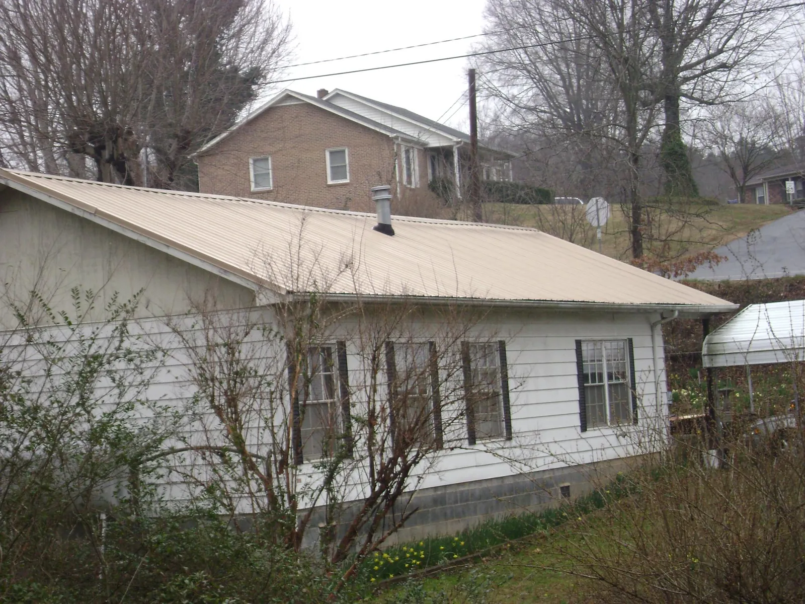 Tan metal roof on a white sided house set into a hillside — Commercial Roofing by Roofing Brothers in Chugwater
